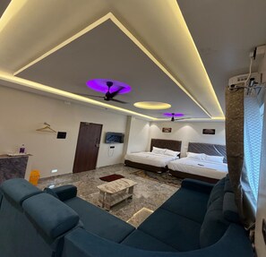 Una moderna camera d'albergo con divano, due letti, televisore e ventilatore a soffitto.