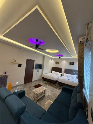 Camera d'albergo con due letti, un divano, un tavolino, ventilatori a soffitto e una televisione.