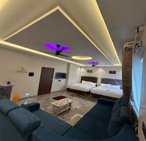 Una camera d'albergo con due letti, un divano, una TV e una ventola a soffitto.