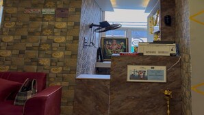 A reception area with a patterned wall, a red chair, a ceiling light fixture, and a framed picture on the wall. - Sasikala Residency  (Madurantakam)