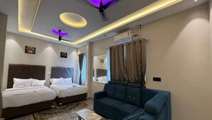 A modern hotel room with a large bed, a sofa, a ceiling fan, and a ceiling light fixture. - Sasikala Residency  (Madurantakam)