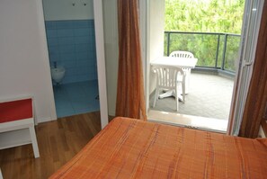 Een kamer met een bed, een klein wit tafeltje, een witte stoel en een balkon met uitzicht op groen.