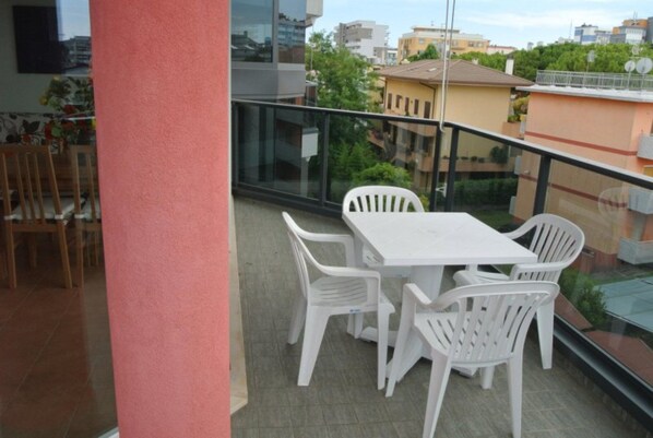 Een balkon met een tafel en stoelen, een glazen hekwerk en uitzicht op gebouwen.