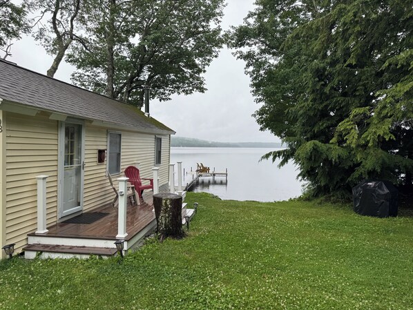 A house with a deck, a red chair, and a dock extending into a lake.