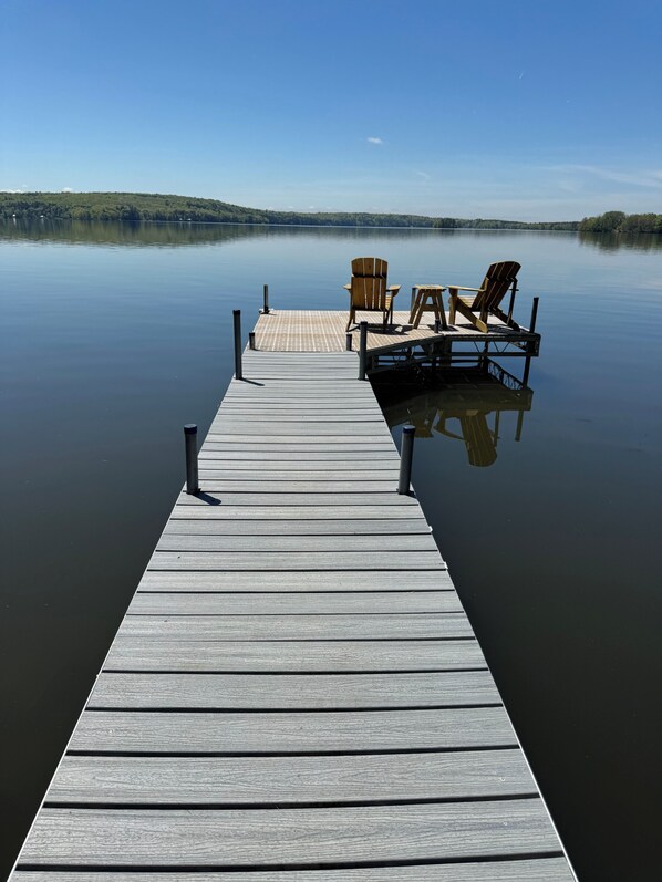 A wooden pier extending into calm water, with two wooden chairs and a table at the end.
