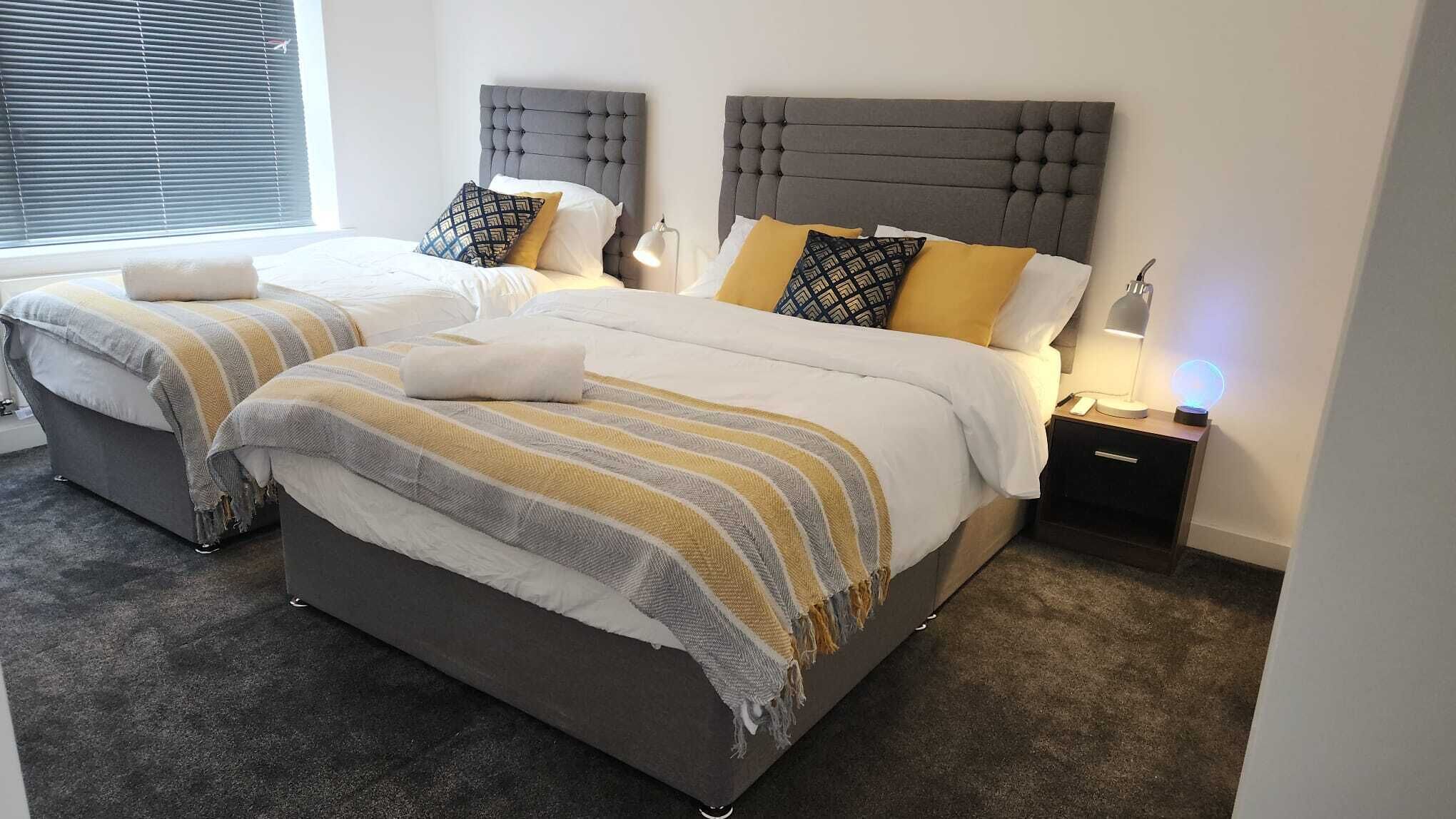 Une chambre double avec deux lits, des têtes de lit grises et des tables de chevet avec des lampes.