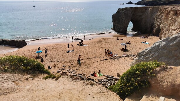 A beach with people, a sailboat, and a large rock formation. - The roch annex (Saint-Pierre-Quiberon)