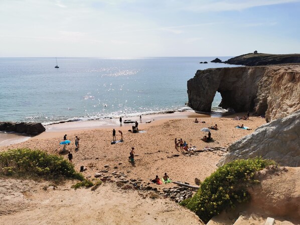 A beach with people, a sailboat, and a large rock formation. - The roch annex (Saint-Pierre-Quiberon)