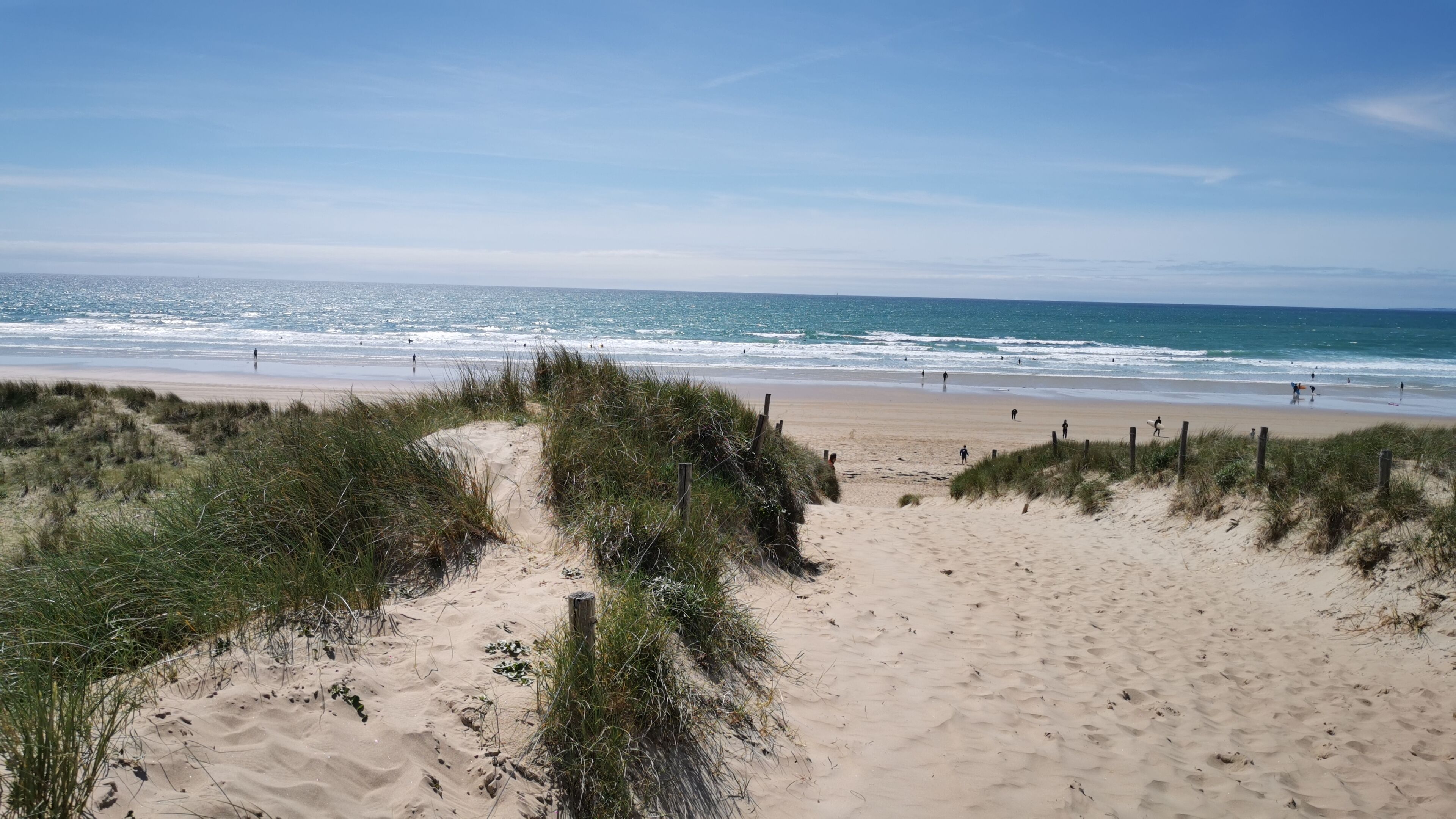 Platja sorrenca amb vistes clares a l'oceà i una zona de dunes herboses.