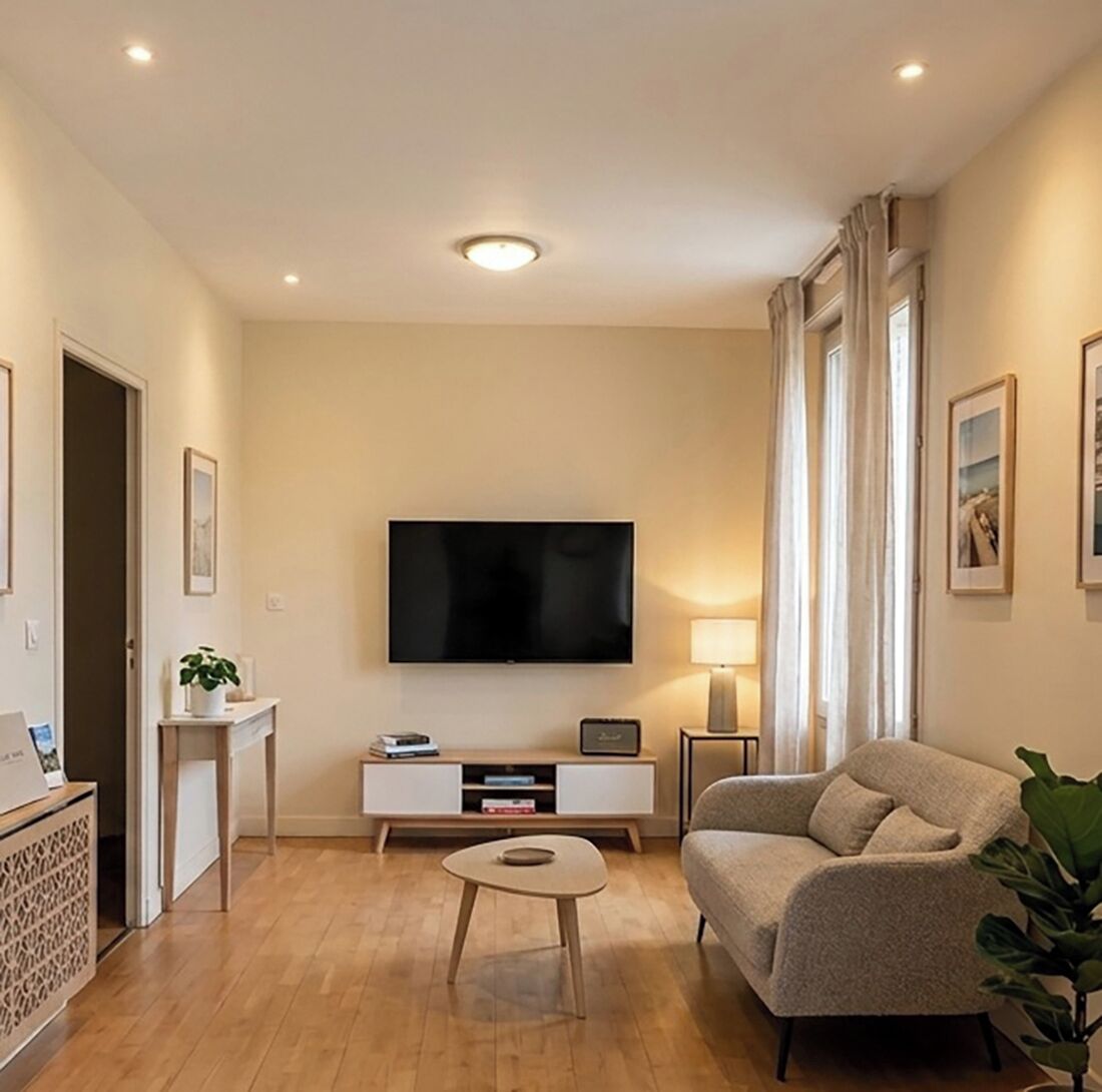 Een moderne woonkamer met een flatscreen televisie, een bank, een salontafel en een bijzettafeltje met een lamp.