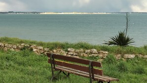 A bench by a body of water with a stone wall in the foreground and a distant shoreline. - The roch annex (Saint-Pierre-Quiberon)