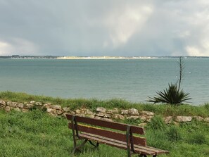 A bench by a body of water with a stone wall in the foreground and a distant shoreline. - The roch annex (Saint-Pierre-Quiberon)