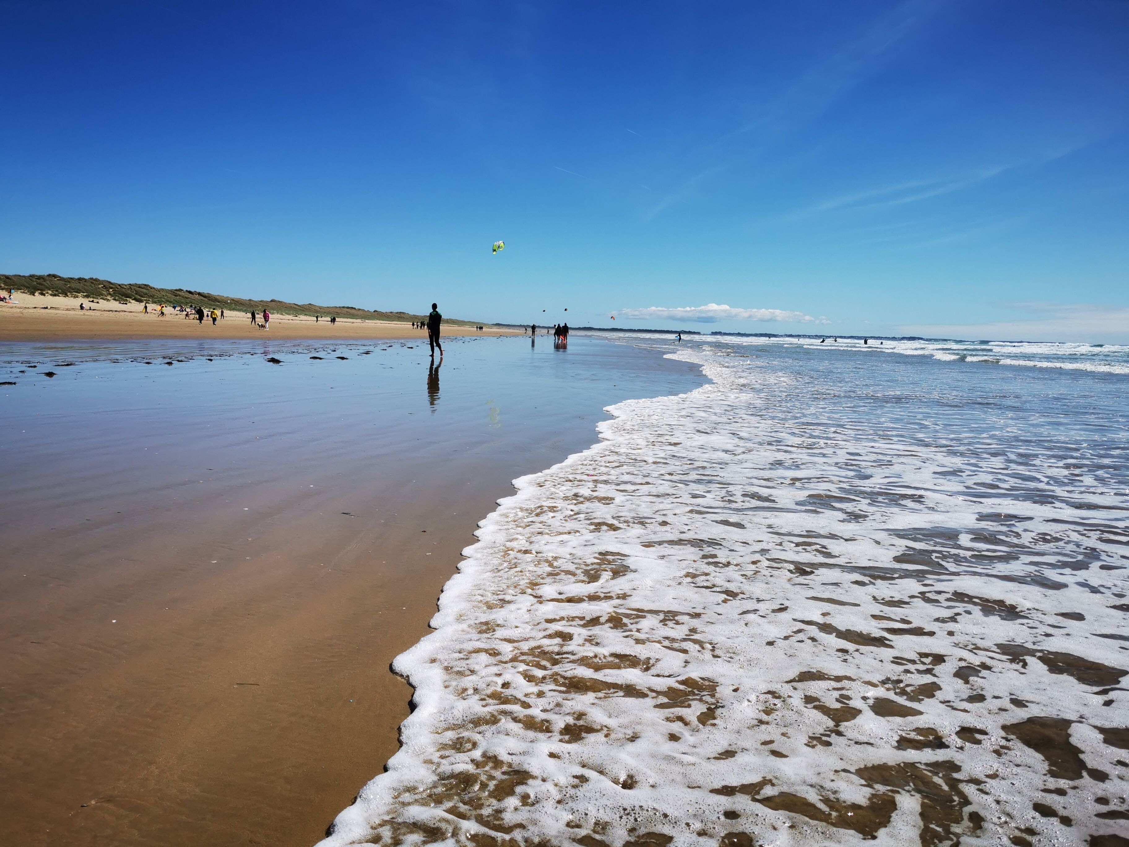 Une plage avec un large rivage sablonneux, des vagues douces et un ciel bleu dégagé.