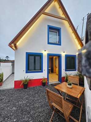 Une maison à deux étages, dotée d’un toit en pente, d’un balcon et d’un petit patio avec une table et des chaises.