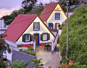 Une maison à deux étages avec un toit rouge, des volets bleus et un petit porche à l’avant.