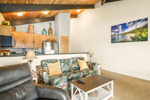 Ein Wohnzimmer mit einer Couch, einem Couchtisch und einer Küchenzeile mit Holzschränken und einem Kühlschrank.