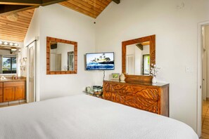 Une chambre à coucher avec un grand lit, une tête de lit en bois, deux miroirs muraux, un téléviseur à écran plat et une commode en bois.