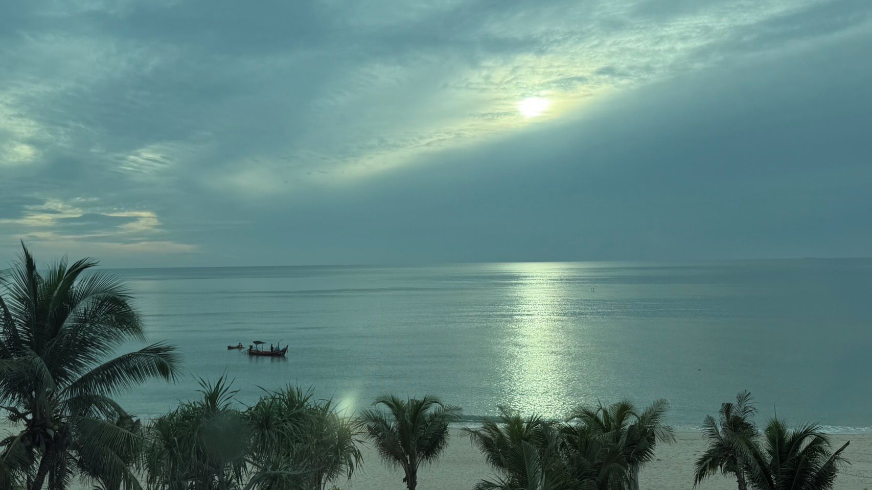 Mar calmo com barco, palmeiras e céu claro.