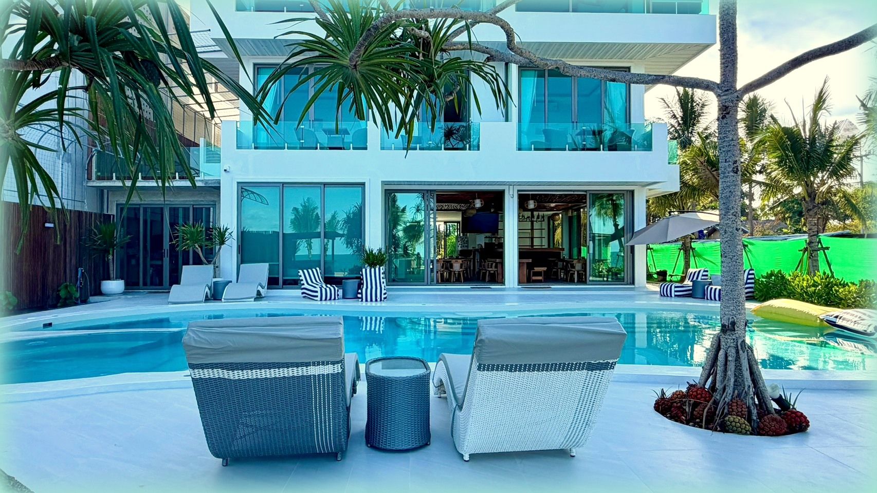 A modern house with a swimming pool, lounge chairs, and a dining area.