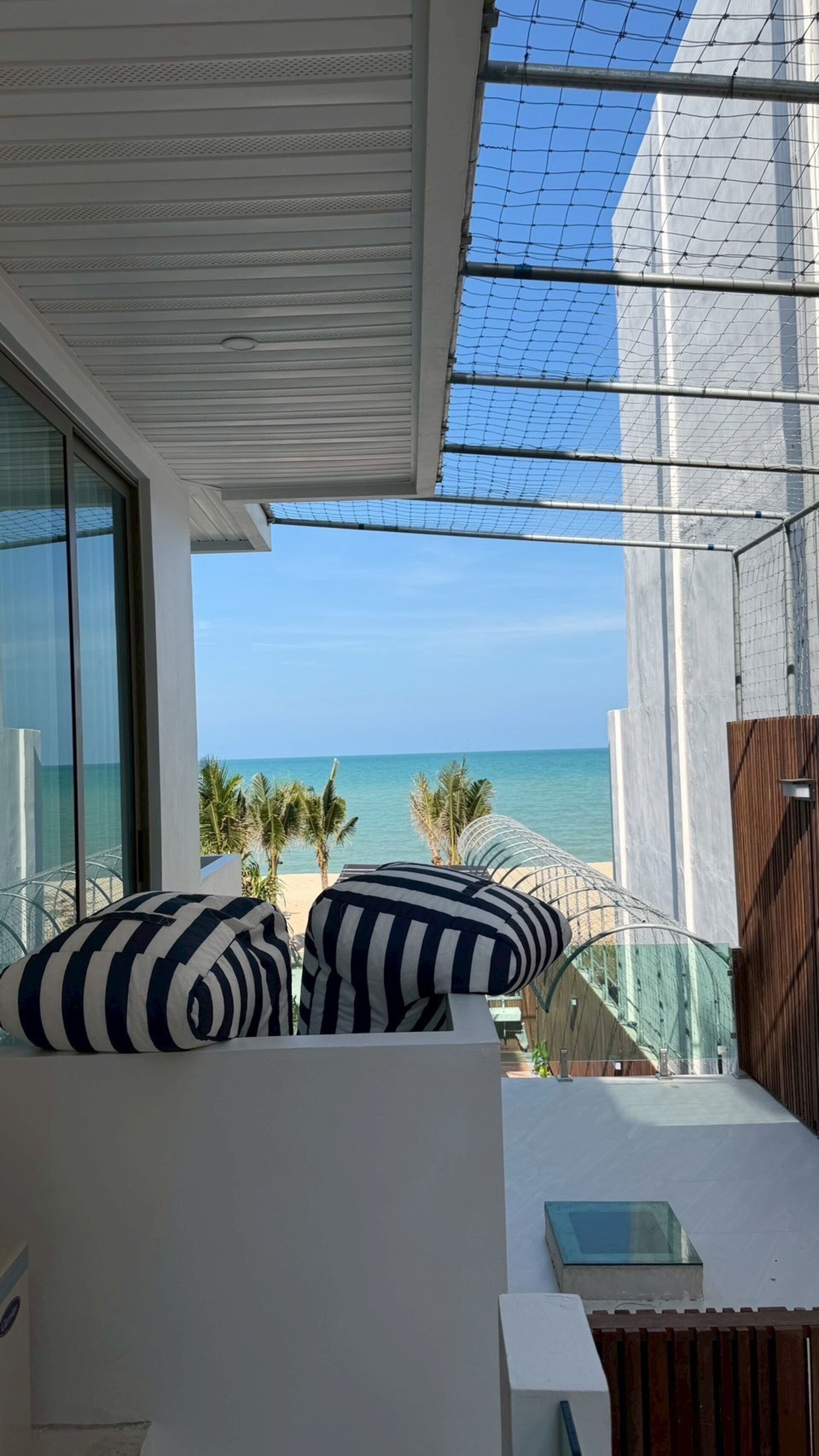 A balcony with a view of the sea, a white ceiling, and a striped pillow.
