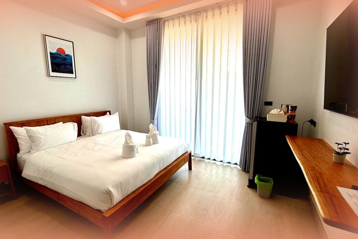 Habitación de hotel con cama, escritorio, televisor y ventana con cortinas.