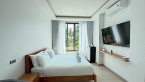 Una moderna camera d'hotel con un ampio letto, una TV a schermo piatto, un tavolino e vista sul verde dalla finestra.