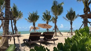 Una spiaggia con palme, una zona sabbiosa e due poltrone in vimini.