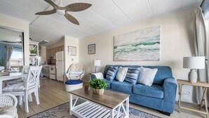 A living room with a blue sofa, white coffee table, and a ceiling fan. - Just listed for rent! Oceanview condo in an oceanfront building with a pool, elevator and assigned parking (Ocean City)