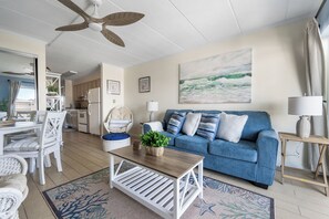 A living room with a blue sofa, white coffee table, and a ceiling fan. - Just listed for rent! Oceanview condo in an oceanfront building with a pool, elevator and assigned parking (Ocean City)