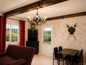 Un coin repas avec une table et des chaises, un lustre, des armoiries sur le mur et une vue par la fenĂȘtre.