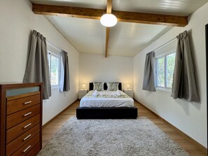 Ein Schlafzimmer mit einem Bett, Nachttischen, einer Kommode und einem Fenster mit Vorhängen.