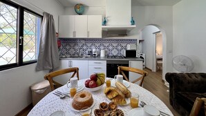 Et kompakt køkken med hvide skabe, flisebeklædt bagvæg og et spiseområde med et bord dækket til morgenmad.