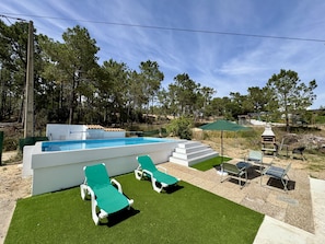 Une piscine au design moderne, entourée de gazon synthétique et de chaises longues.
