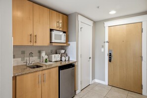 A compact kitchen with wooden cabinets, a microwave, a dishwasher, and a white door. - Studio in Elation at Sandestin Golf and Beach Resort! (Miramar Beach)