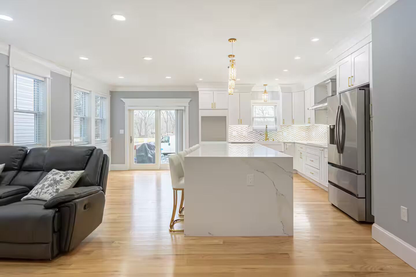 A modern kitchen with a central island, stainless steel appliances, and a grey sofa.