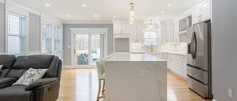 A modern kitchen with a central island, stainless steel appliances, and a grey sofa.