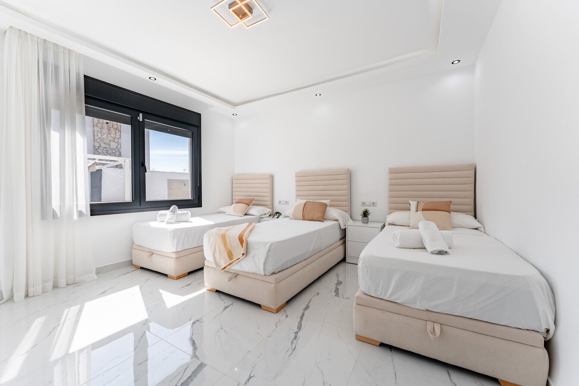 Quarto moderno com três camas, uma janela grande e piso de mármore.