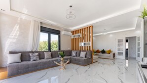 Een moderne woonkamer met een grijze hoekbank, een glazen salontafel en een houten accentmuur.