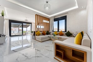Ein modernes Wohnzimmer mit einer Eckcouch, einem Glastisch und Blick auf die Stadt.