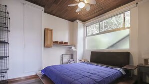 Ein Schlafzimmer mit Bett, Deckenventilator, Fenster und Ablagefläche.