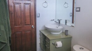 Ein Badezimmer mit Holztür, Waschbecken, Toilette und Spiegel.