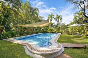 Piscina com borda de tijolos, cercada por grama e palmeiras.