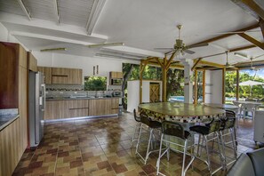 Cozinha com ilha central, banquetas, ventiladores de teto e vista para o exterior.