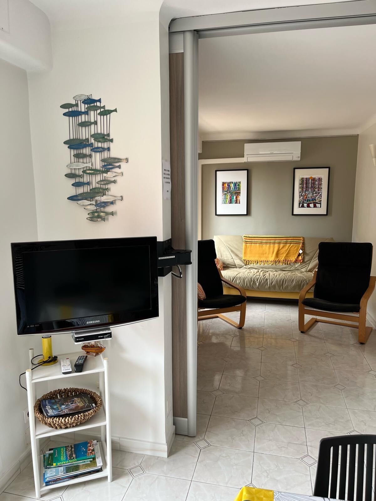A living room with a flat-screen TV, a wall-mounted fish sculpture, a sofa, and a coffee table.