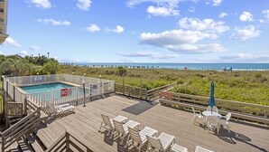 A wooden deck with pool, chairs, and tables overlooking a beach. - Chateau By The Sea-Oceanfront-Sleeps4-2b/2b-King Beds-Laundry-Kitchen (North Myrtle Beach)