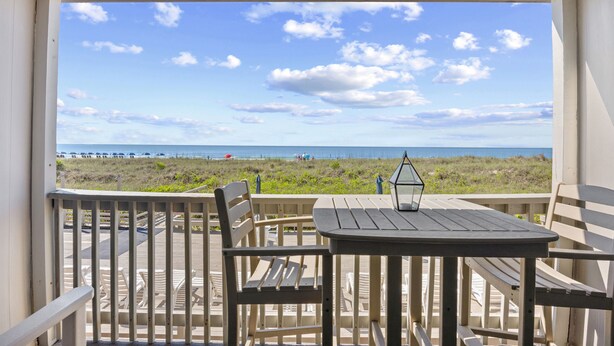A balcony with a table and chairs, overlooking a beach with people and umbrellas. - Chateau By The Sea-Oceanfront-Sleeps4-2b/2b-King Beds-Laundry-Kitchen (North Myrtle Beach)