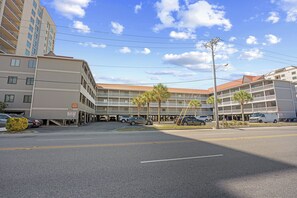 A multi-story hotel with a parking lot, palm trees, and a clear sky. - Chateau By The Sea-Oceanfront-Sleeps4-2b/2b-King Beds-Laundry-Kitchen (North Myrtle Beach)