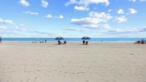 A beach with two umbrellas, a clear sky, and the ocean in the background. - Chateau By The Sea-Oceanfront-Sleeps4-2b/2b-King Beds-Laundry-Kitchen (North Myrtle Beach)