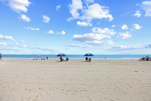 A beach with two umbrellas, a clear sky, and the ocean in the background. - Chateau By The Sea-Oceanfront-Sleeps4-2b/2b-King Beds-Laundry-Kitchen (North Myrtle Beach)