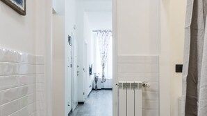 Ein Flur mit weiß gefliesten Wänden, einem Heizkörper und einer Tür zu einem Zimmer.
